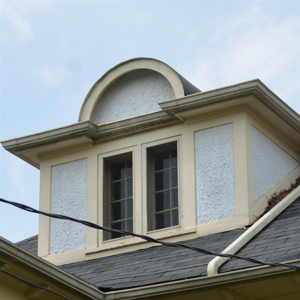 Dormer window with a semi-circle arch above, wood trim in buttery yellow and white. Building surface is white stucco